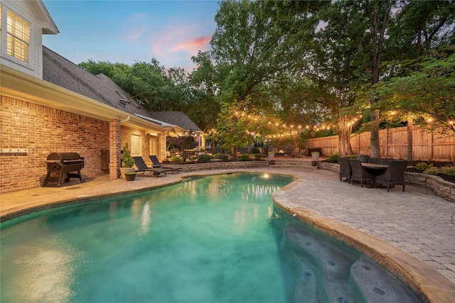 pool at dusk with fence, a fenced in pool, area for grilling, and a patio area