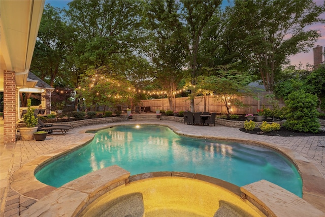 pool at dusk with a fenced backyard, a patio, and a pool with connected hot tub