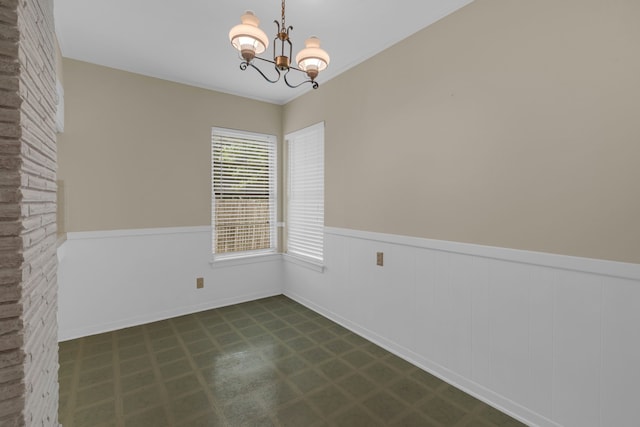 spare room with dark floors, ornamental molding, wainscoting, and a notable chandelier