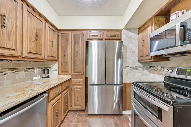 kitchen featuring light stone counters, brown cabinetry, stainless steel appliances, and backsplash