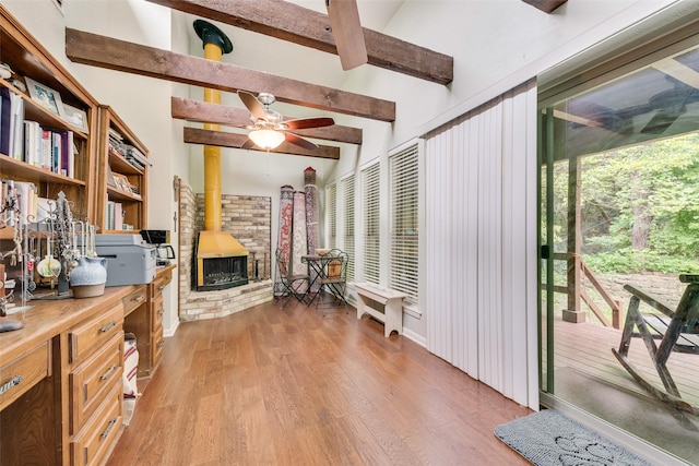 office with a ceiling fan, lofted ceiling with beams, light wood-style flooring, and a wood stove