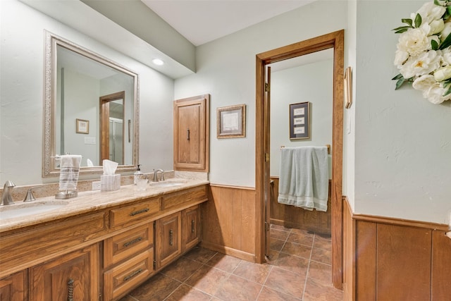 bathroom with wooden walls, double vanity, wainscoting, and a sink