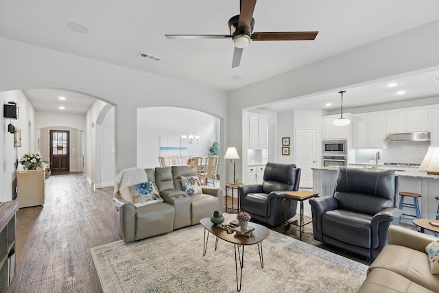 living area with arched walkways, ceiling fan with notable chandelier, recessed lighting, wood finished floors, and visible vents