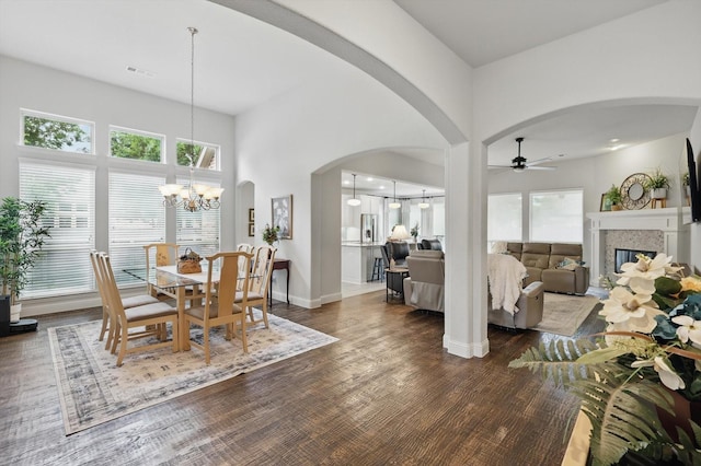 dining space with arched walkways, a glass covered fireplace, ceiling fan with notable chandelier, dark wood-type flooring, and visible vents