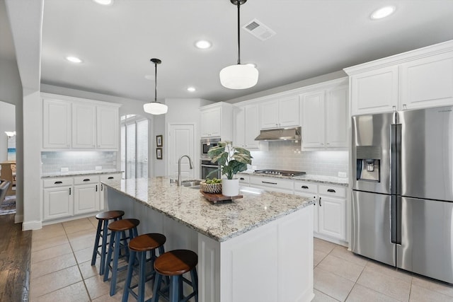 801 Patio St, Little Elm, TX 76227 - kitchen featuring stainless steel appliances, under cabinet range hood, a sink, decorative backsplash, and light tile patterned floors