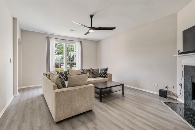 6401 Marlar Ln, The Colony, TX 75056 - living room featuring a premium fireplace, ceiling fan, light wood-style flooring, baseboards, and arched walkways