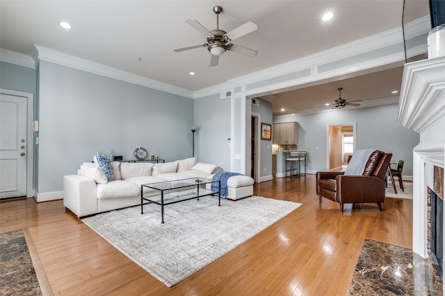living room featuring crown molding, light wood-style floors, baseboards, ceiling fan, and a fireplace with flush hearth