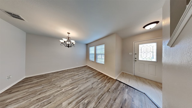 foyer entrance featuring baseboards, a notable chandelier, wood finished floors, and visible vents