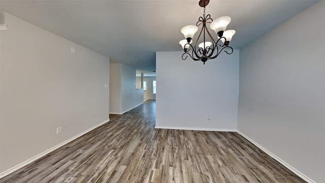 unfurnished dining area with baseboards, wood finished floors, and a chandelier