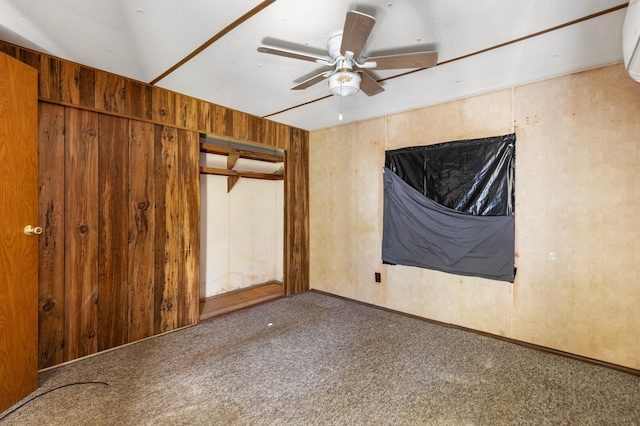 unfurnished room with wooden walls, carpet floors, and ceiling fan