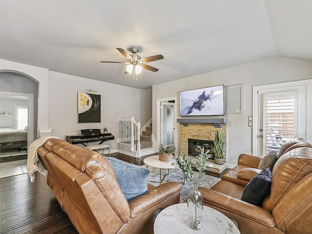 living area featuring ceiling fan, arched walkways, a fireplace, vaulted ceiling, and dark wood-type flooring