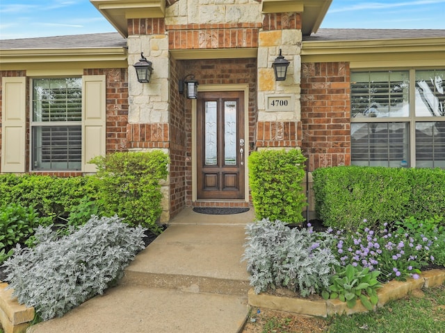 doorway to property featuring brick siding, roof with shingles, and stone siding