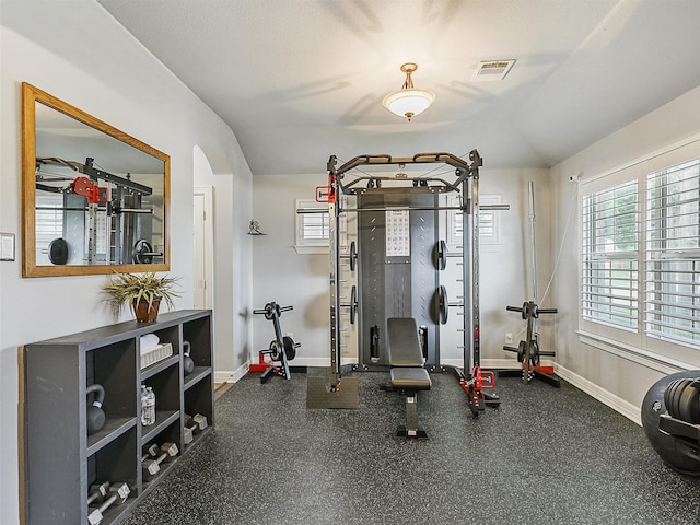 workout room with arched walkways, baseboards, vaulted ceiling, and a healthy amount of sunlight