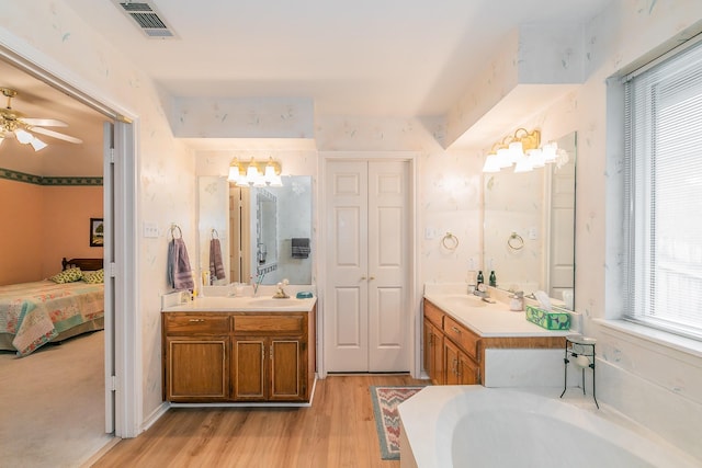 ensuite bathroom with visible vents, wood finished floors, two vanities, a sink, and connected bathroom