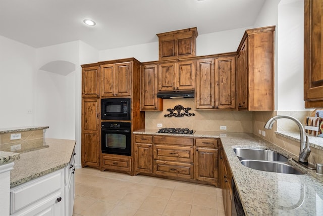 kitchen featuring light stone countertops, a sink, decorative backsplash, under cabinet range hood, and black appliances