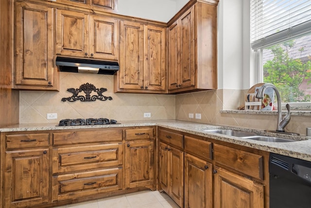 kitchen with under cabinet range hood, brown cabinets, a sink, and dishwasher