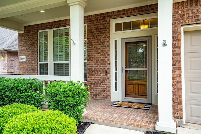 entrance to property featuring a porch, brick siding, and a garage