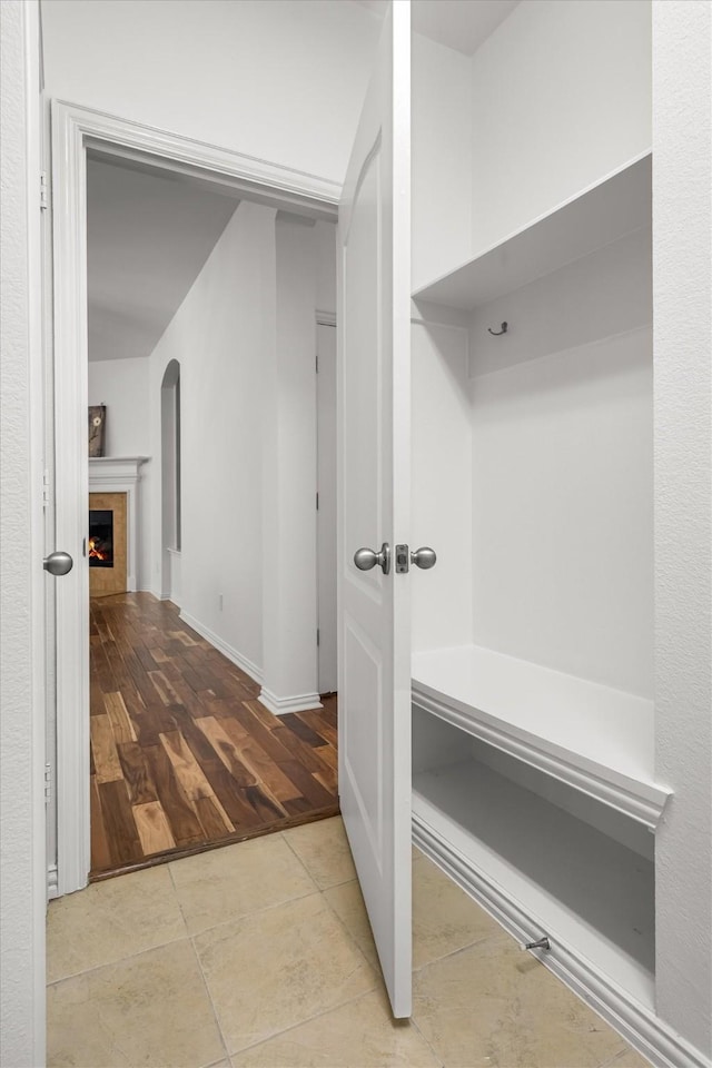 mudroom with arched walkways, a warm lit fireplace, and tile patterned flooring