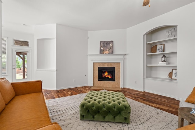 living area with a tiled fireplace, wood finished floors, visible vents, and built in shelves