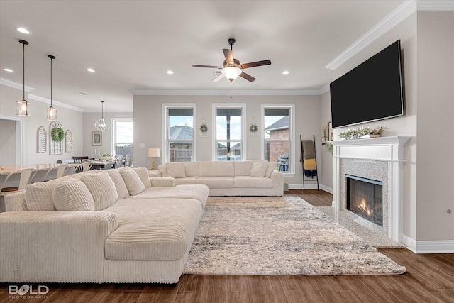 living area with ornamental molding, wood finished floors, baseboards, ceiling fan, and a warm lit fireplace