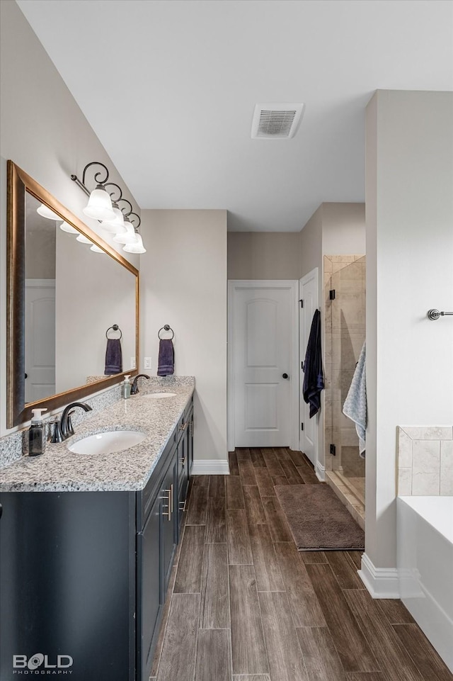 bathroom with double vanity, visible vents, a stall shower, wood finished floors, and a sink