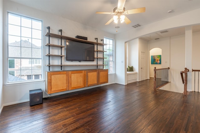 unfurnished living room with ceiling fan, visible vents, arched walkways, baseboards, and dark wood-type flooring