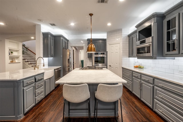 kitchen featuring appliances with stainless steel finishes, a sink, decorative backsplash, a kitchen island, and gray cabinetry