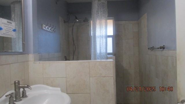 bathroom with a sink, tile walls, and tiled shower