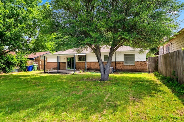 rear view of house featuring a yard, brick siding, and a fenced backyard