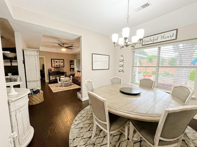 dining space featuring visible vents, a raised ceiling, baseboards, ceiling fan with notable chandelier, and dark wood-type flooring
