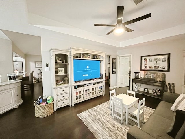 living area with a raised ceiling, a ceiling fan, wood finished floors, and visible vents