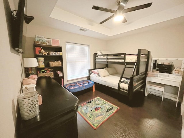 bedroom with visible vents, ceiling fan, wood finished floors, and a tray ceiling