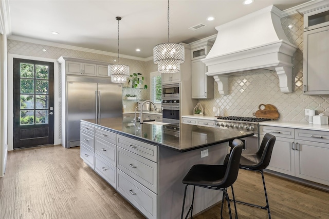 kitchen featuring visible vents, crown molding, a sink, custom exhaust hood, and built in appliances