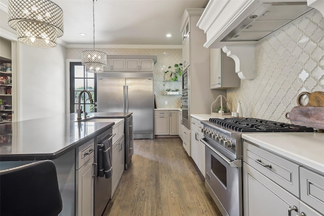 kitchen featuring crown molding, a sink, built in appliances, a chandelier, and premium range hood