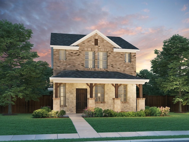 traditional-style home featuring a porch, roof with shingles, fence, a yard, and stone siding