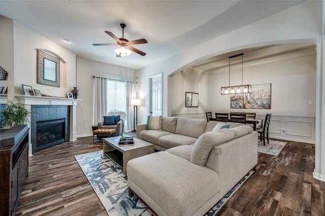 living room with arched walkways, ceiling fan, a fireplace, and dark wood finished floors