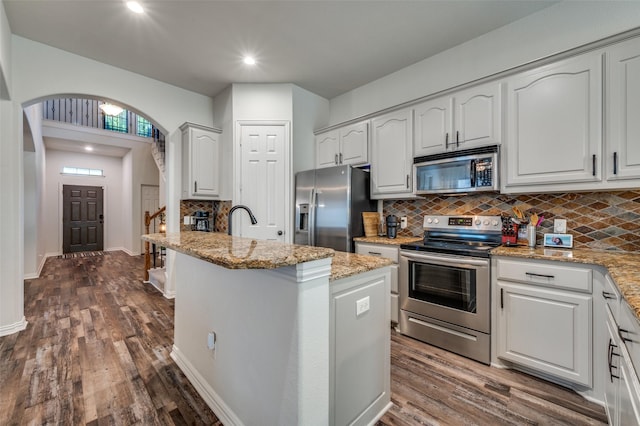 kitchen with arched walkways, white cabinets, stainless steel appliances, and dark wood-type flooring