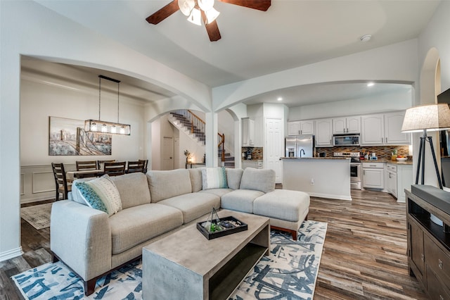 living room with ceiling fan, arched walkways, dark wood finished floors, stairs, and recessed lighting