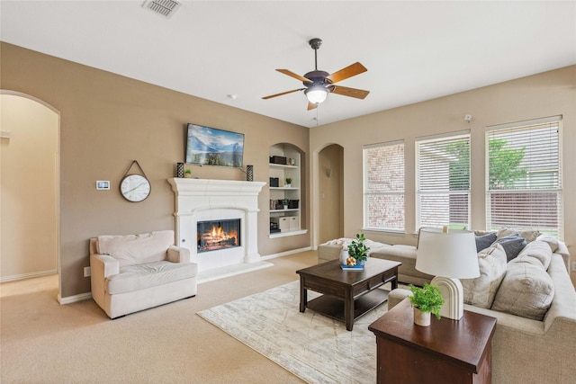 living room featuring ceiling fan, light carpet, arched walkways, built in features, and visible vents