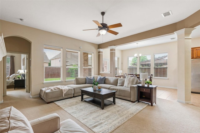 living area featuring visible vents, decorative columns, light carpet, arched walkways, and a ceiling fan