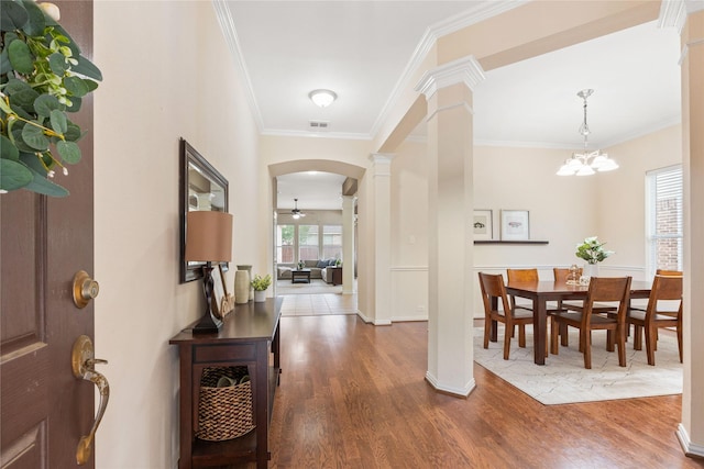 entryway featuring crown molding, arched walkways, decorative columns, and wood finished floors
