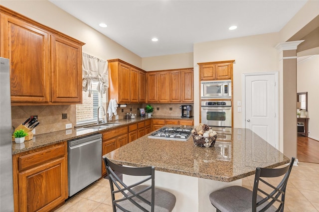 kitchen featuring brown cabinetry, a breakfast bar area, a sink, stone counters, and appliances with stainless steel finishes