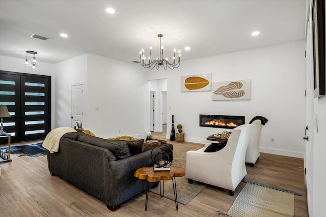 living area featuring visible vents, a glass covered fireplace, wood finished floors, recessed lighting, and a chandelier