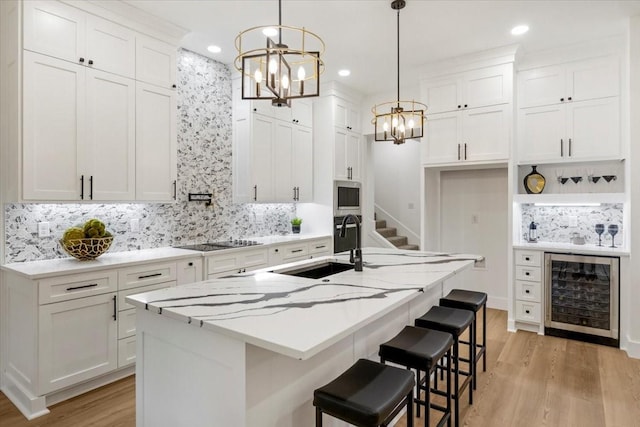 kitchen with a sink, a chandelier, stainless steel microwave, tasteful backsplash, and wine cooler