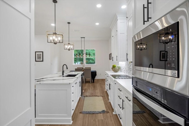 kitchen with an inviting chandelier, light countertops, white cabinetry, light wood-style flooring, and stainless steel appliances