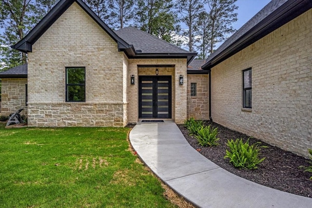 view of exterior entry featuring a lawn, roof with shingles, and stone siding