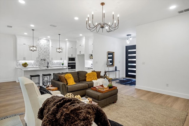 living area featuring baseboards, a notable chandelier, light wood-style flooring, and visible vents