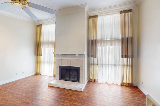 unfurnished living room with crown molding, wood finished floors, a fireplace, baseboards, and a ceiling fan