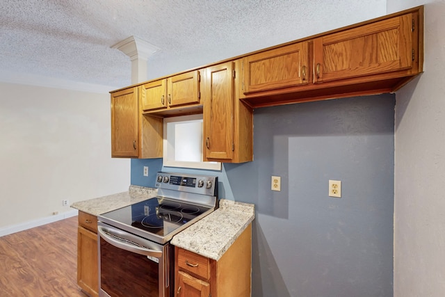 kitchen featuring brown cabinetry, wood finished floors, baseboards, a textured ceiling, and stainless steel electric range oven