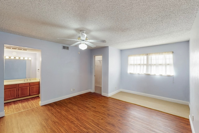 unfurnished bedroom featuring a textured ceiling, visible vents, light wood-type flooring, a sink, and baseboards